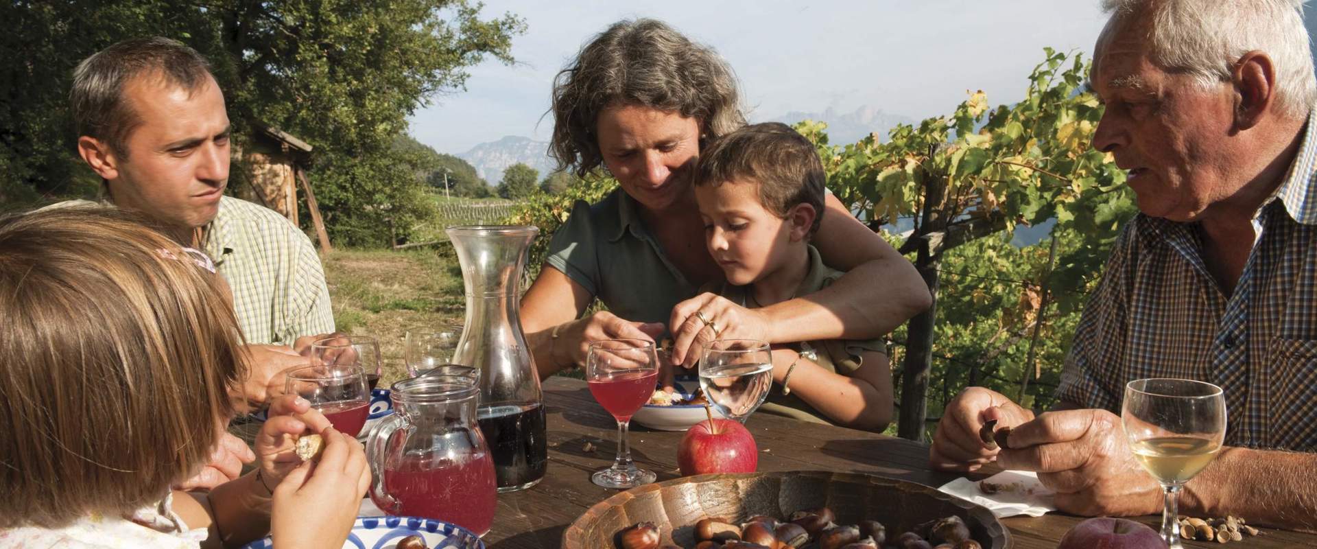 Family sitting at the table outside, eating chestnuts and drinking cider.