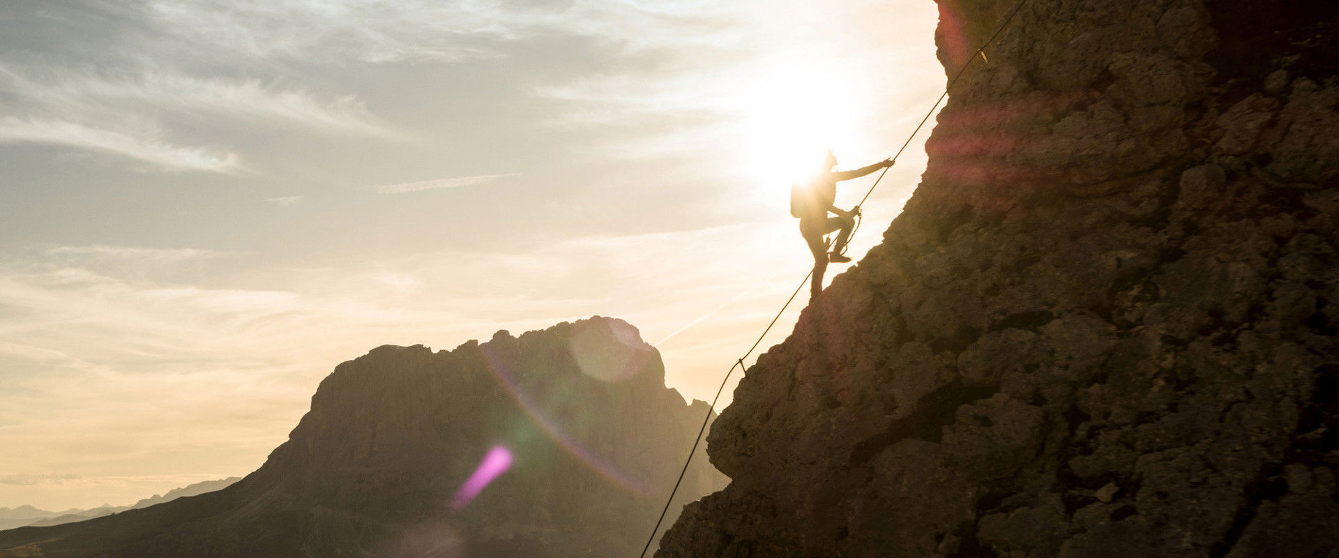 A man holds on to the via ferrata rope and walks up the mountain.