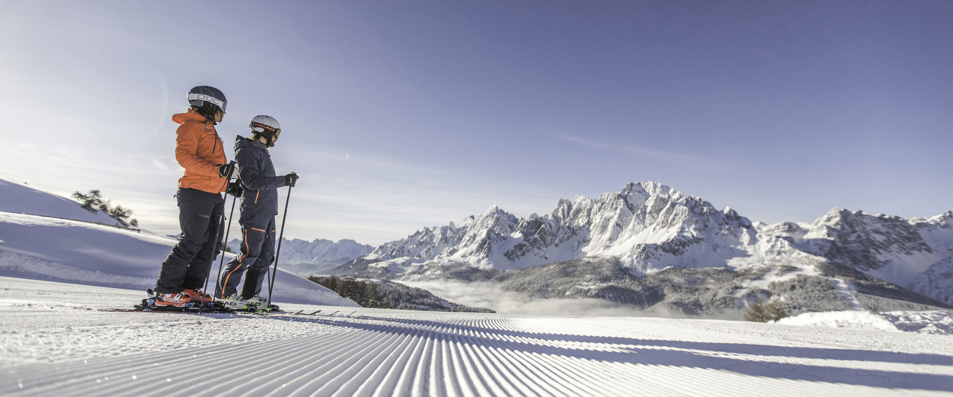 Skiers 2 skiers stand at the edge of the freshly prepared ski slope.