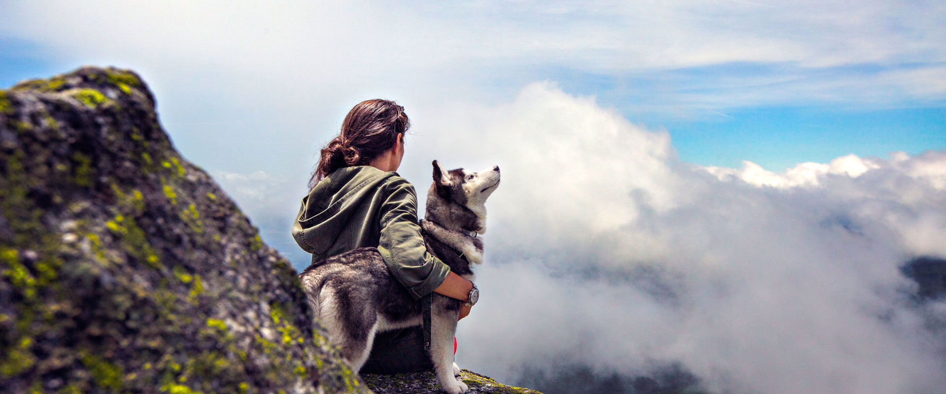 Hiking with dog Woman sitting with her dog on a stone on a mountain.