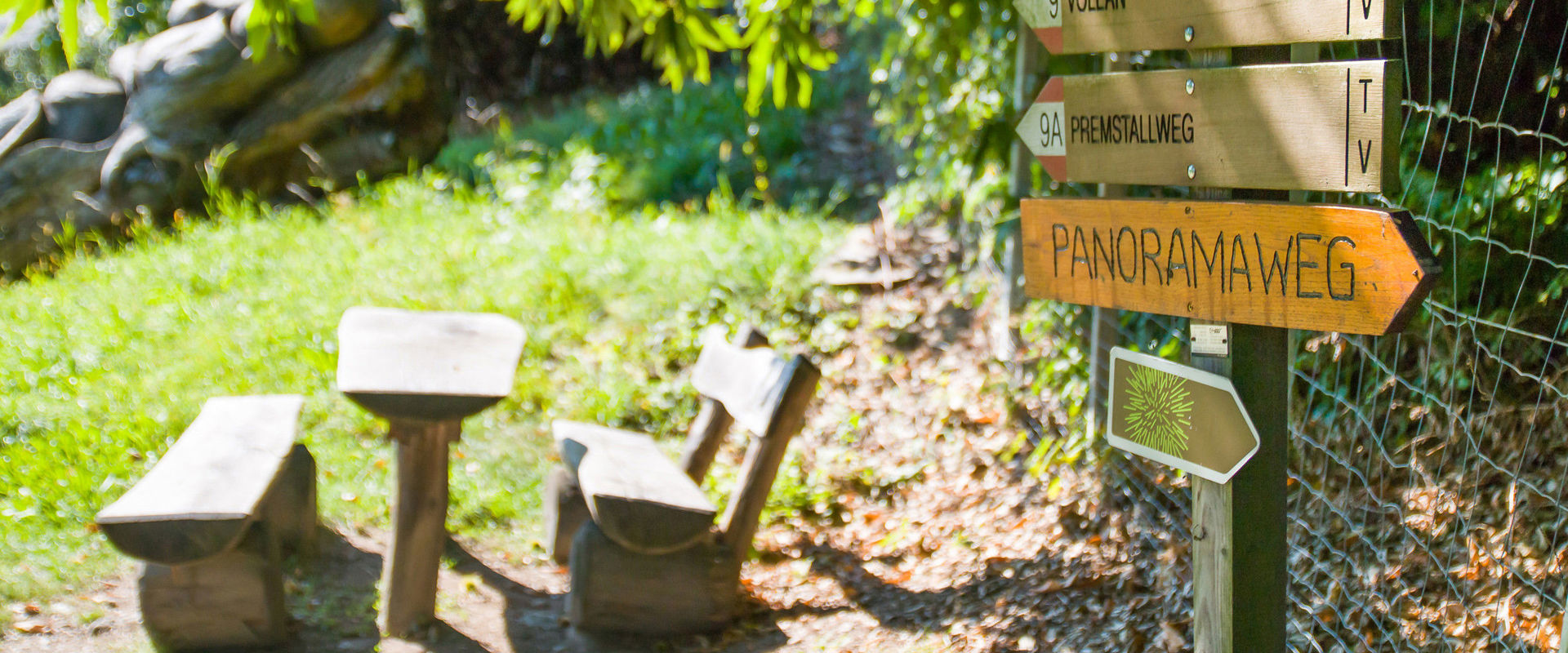 Chestnut path Völlan Signpost and bench under a shady tree.