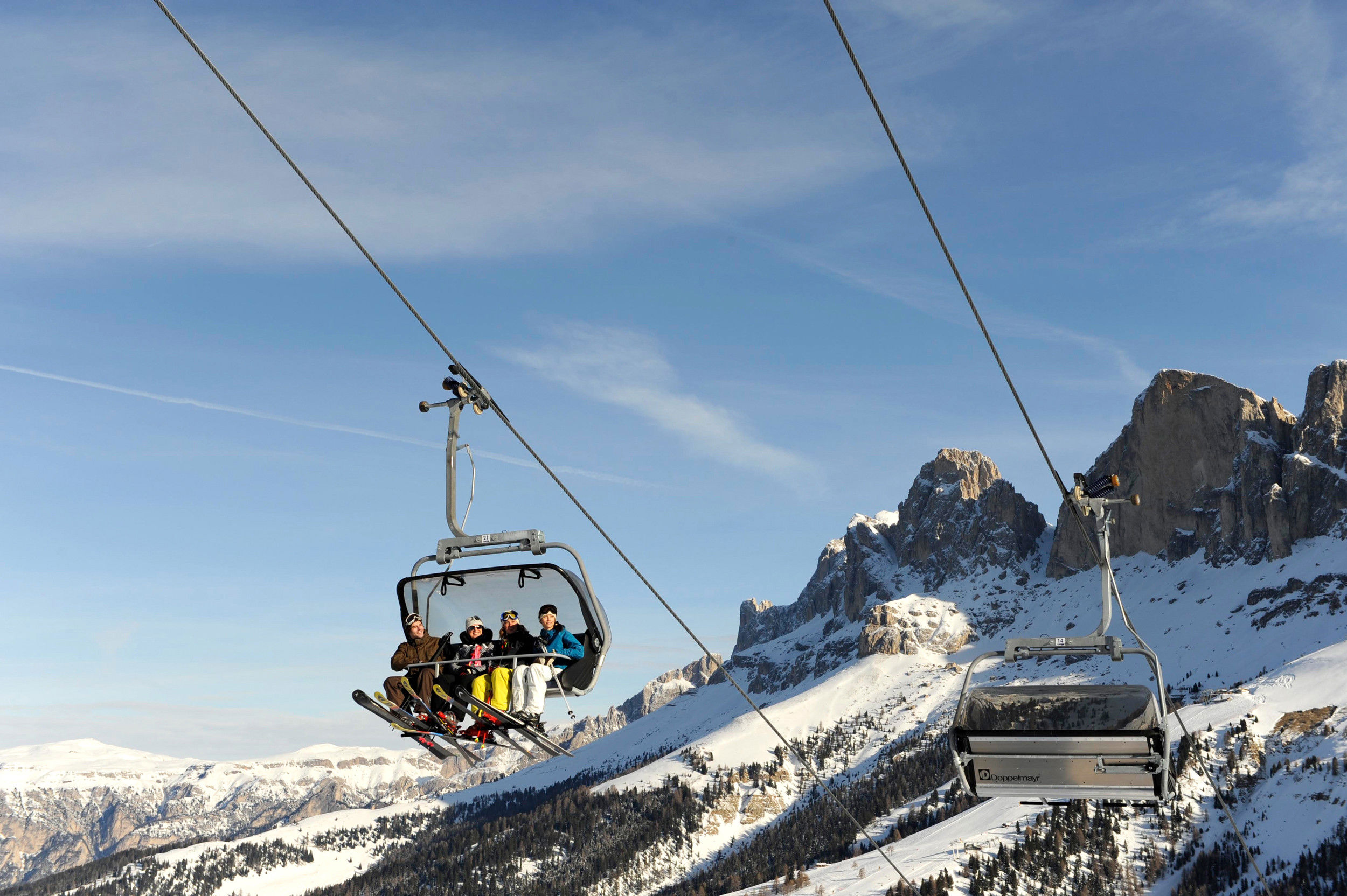 Four skiers in a chairlift in front of a mountain landscape with blue sky.