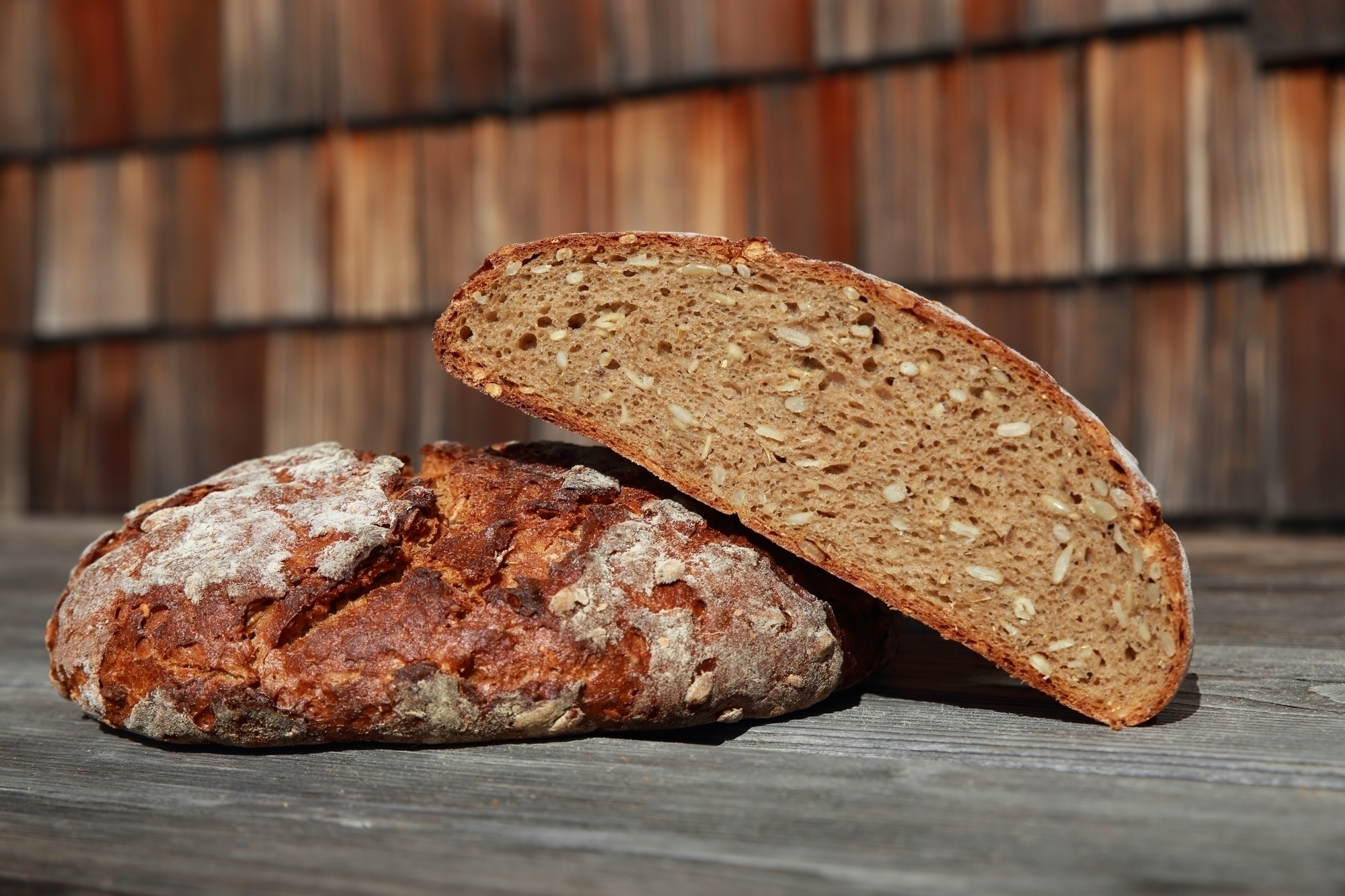 A whole loaf and half a loaf of stone-baked bread are lying on a wooden table in front of the Brixner Hütte.