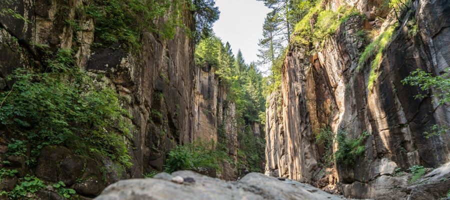 To the left and right of the picture, you can see reddish, steeply rising rock faces overgrown with a few trees.