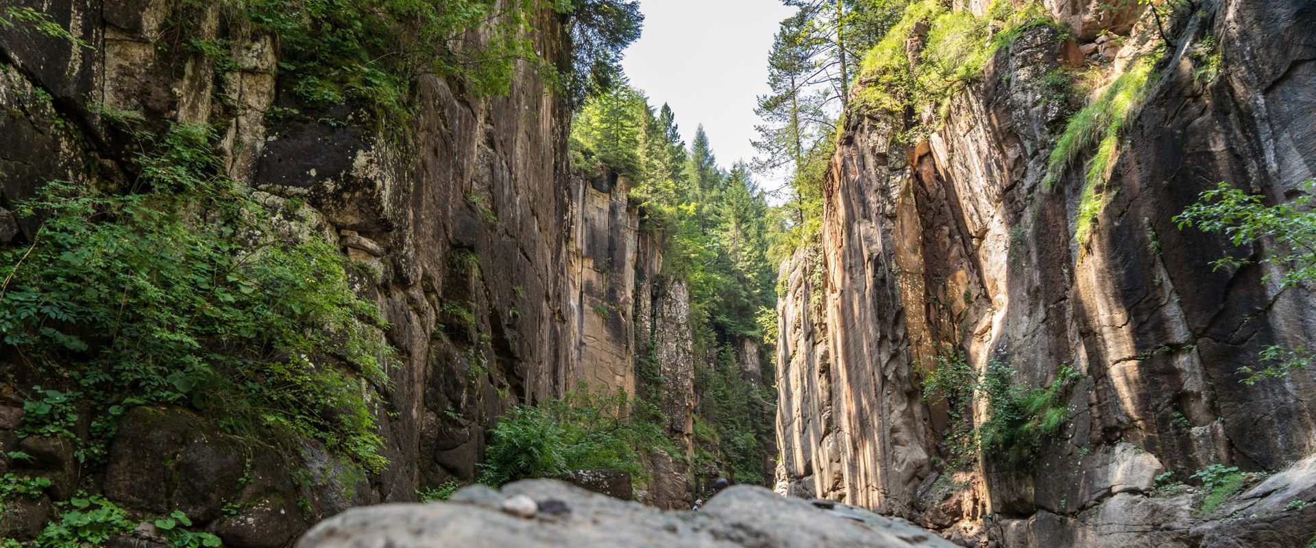 To the left and right of the picture, you can see reddish, steeply rising rock faces overgrown with a few trees.