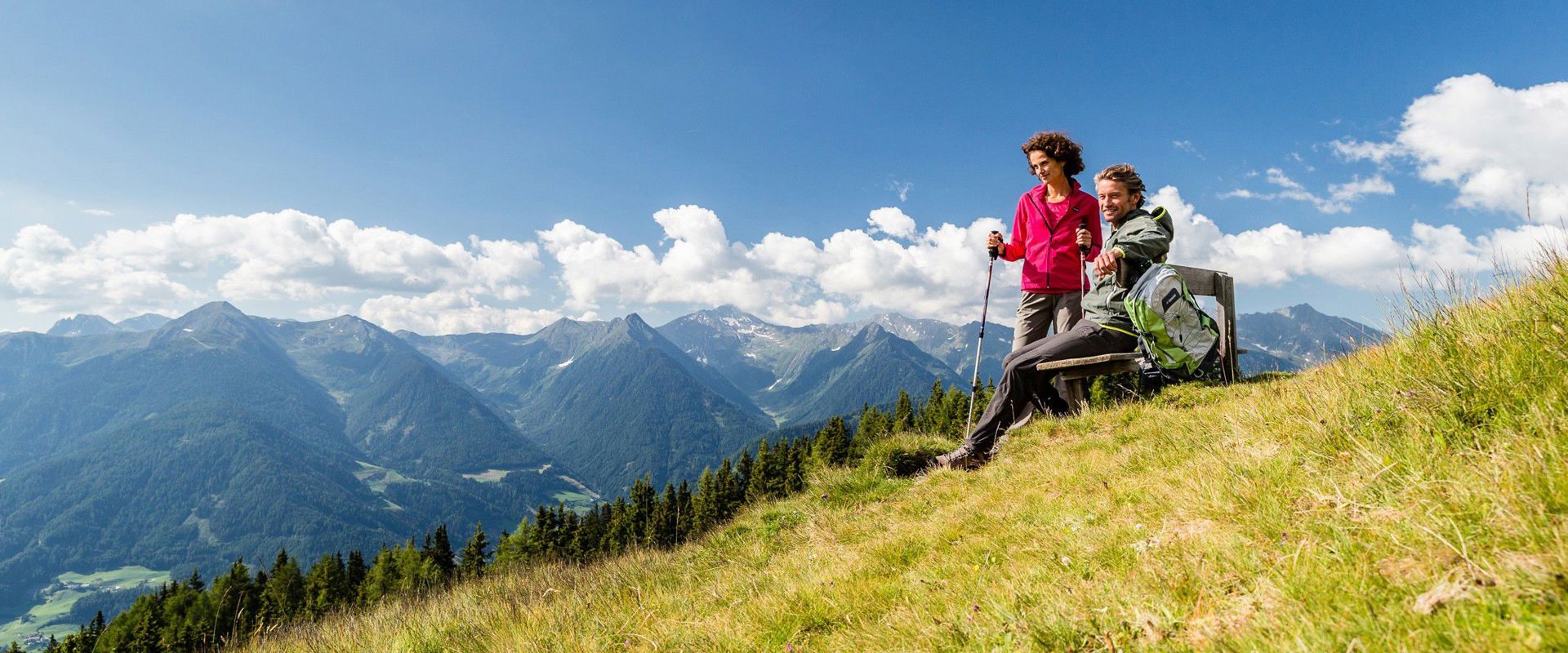 Two hikers resting on a bench along the path leading to the Rosskopf in Sterzing.