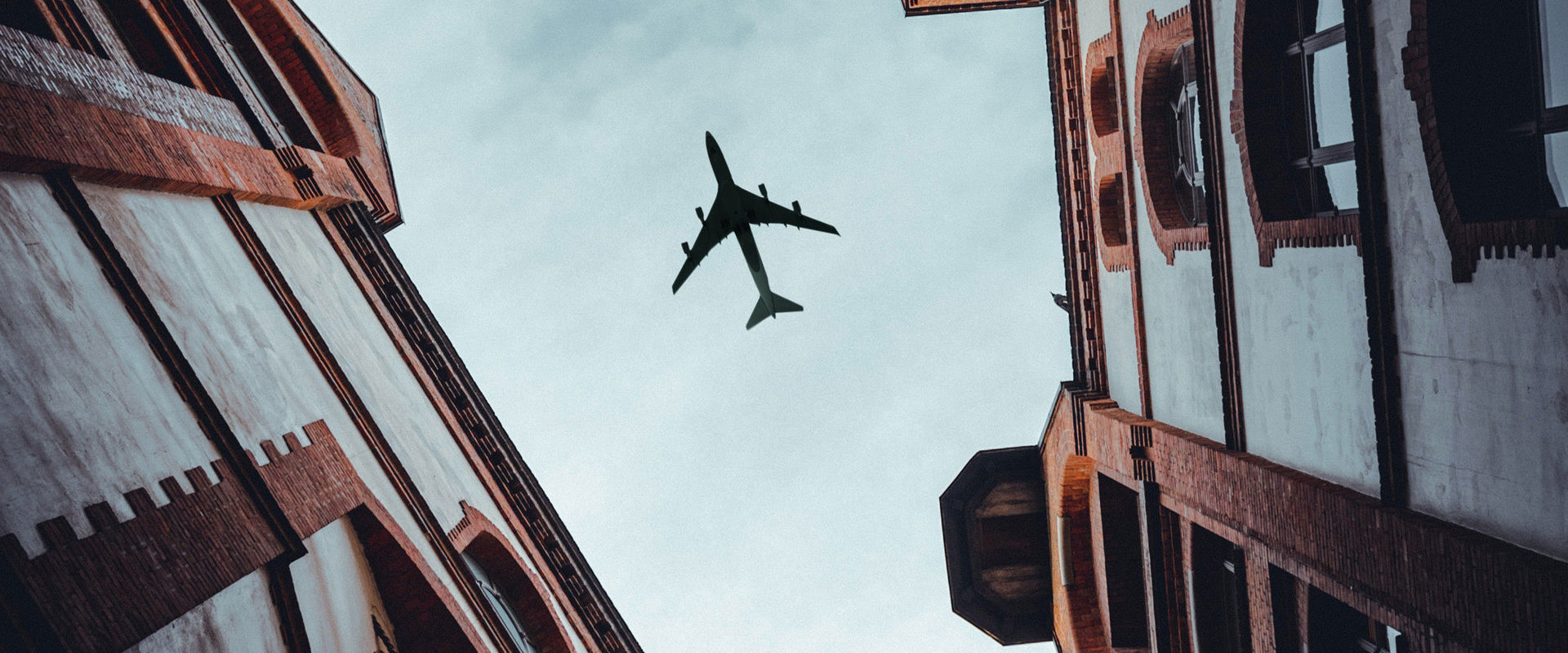 Photo of an aeroplane from below between the houses of a city alley.