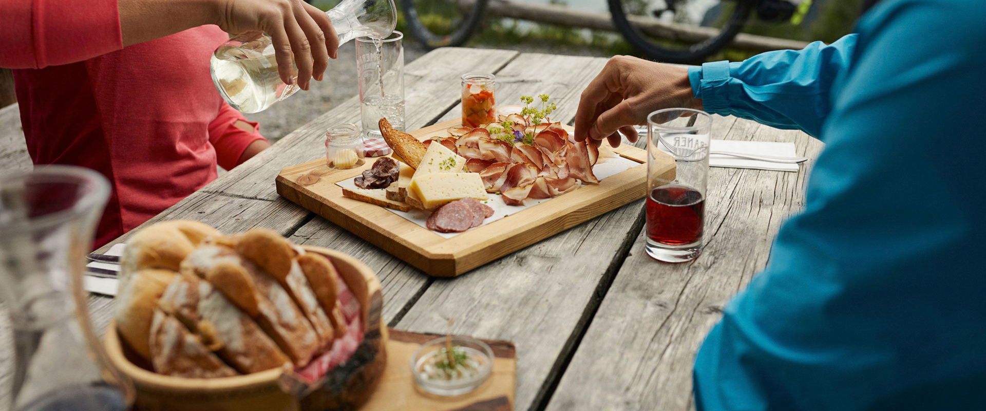Bikers sit on a wooden table and eat a snack.