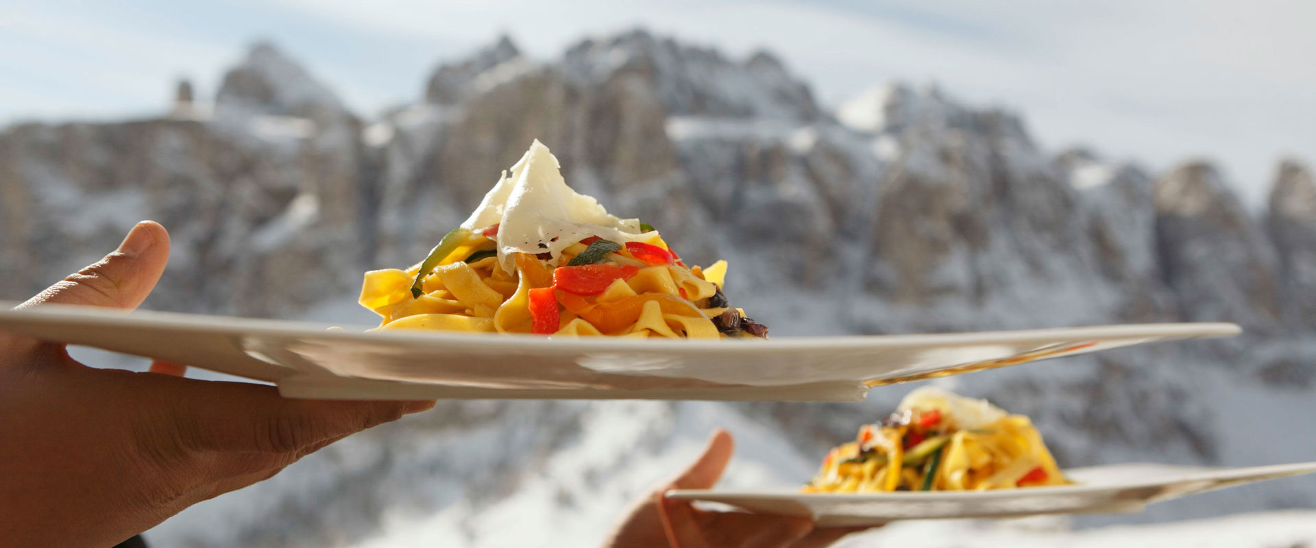 A waiter serves 2 pasta dishes in front of a wintry mountain backdrop.