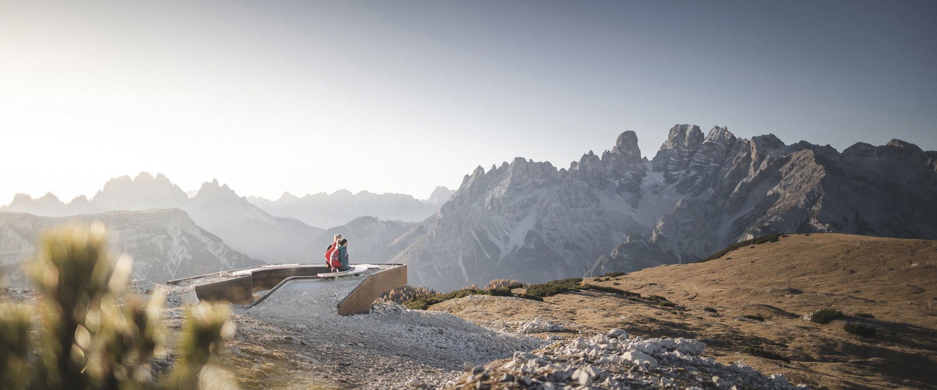 A couple sits at a vantage point and looks out over the bare rocks of the Dolomites.