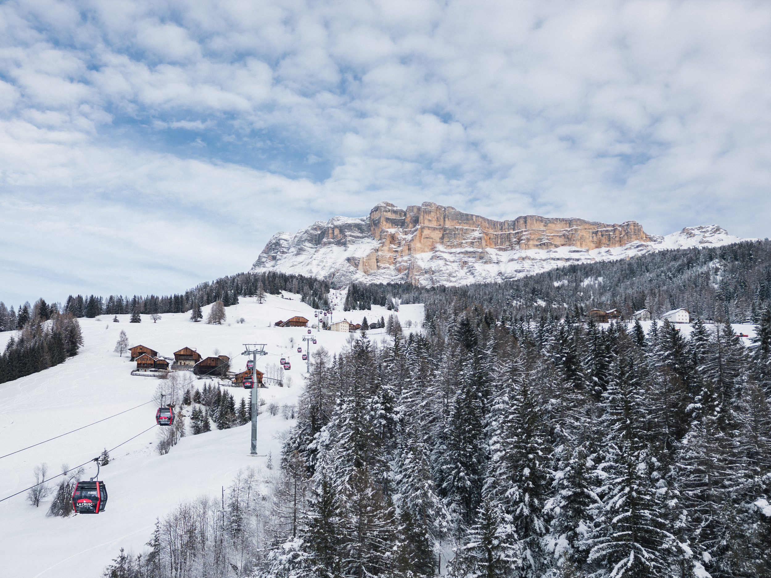 Cable car and mountain farms at the foot of snow-covered mountain peaks in Abtei