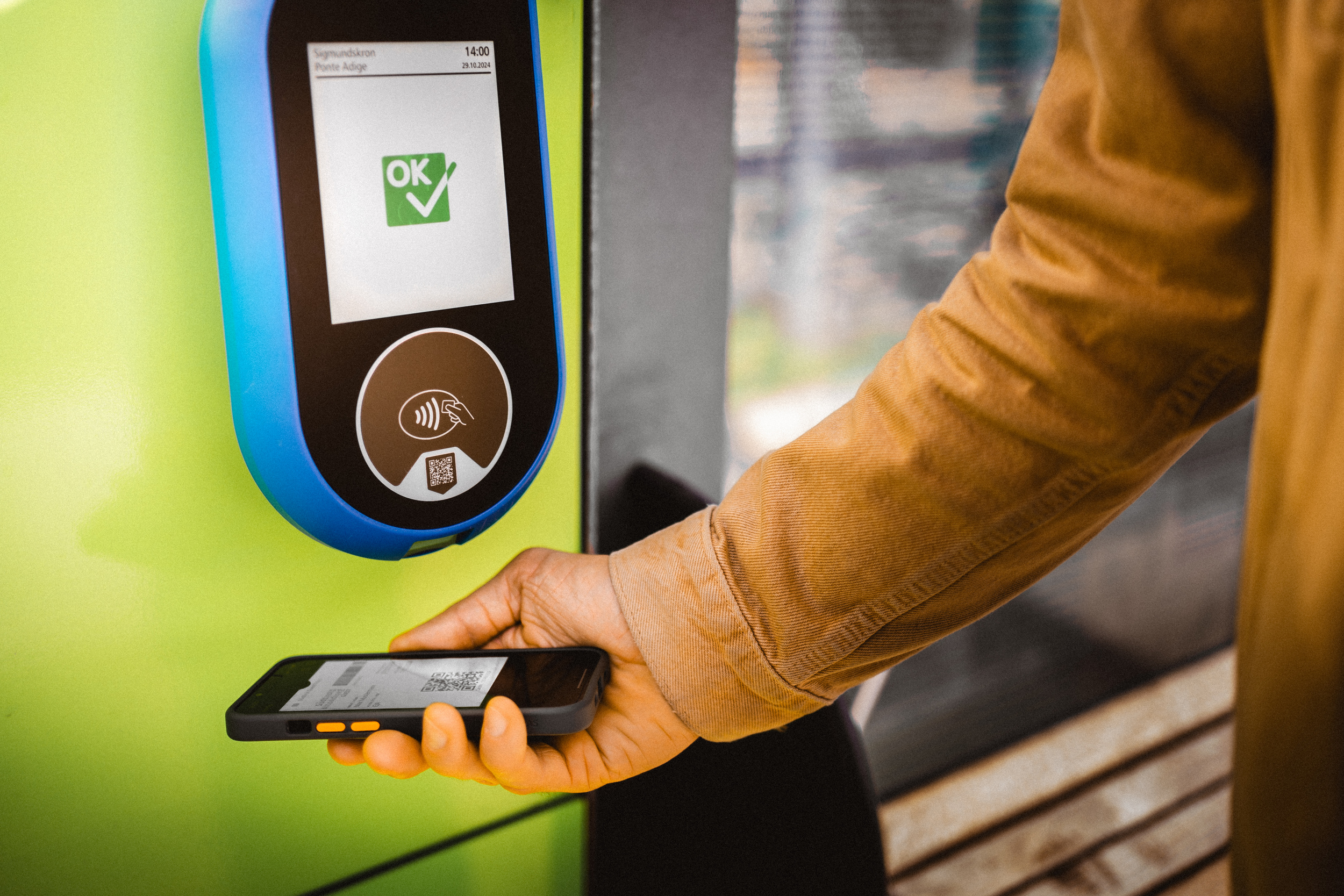 Hand holds public transport card on a mobile phone to a device for validation