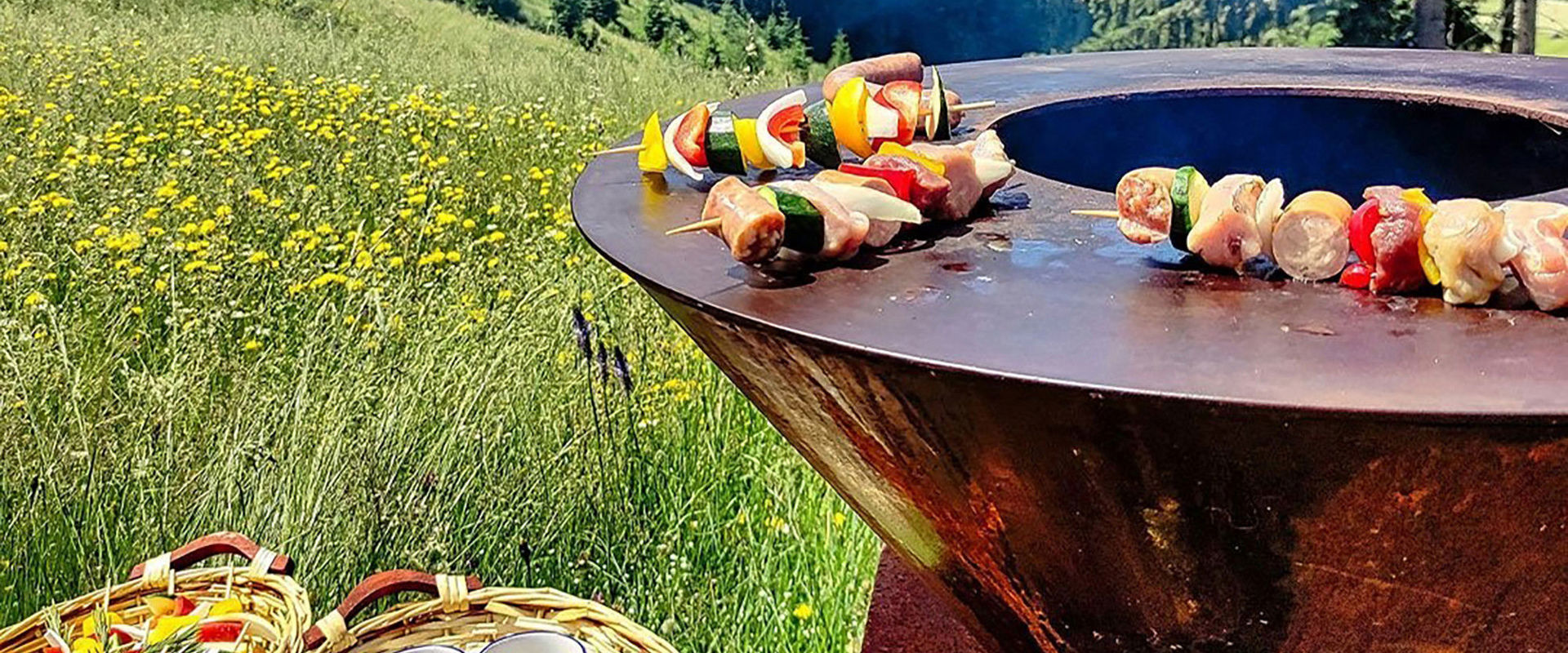 The barbecue is in the middle of the meadow with skewers on it.