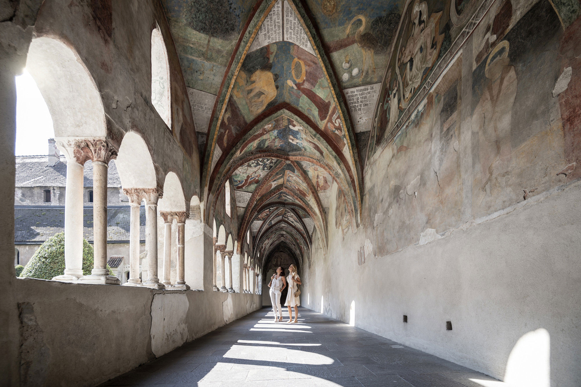 Two women admire the frescoes of the cloister.