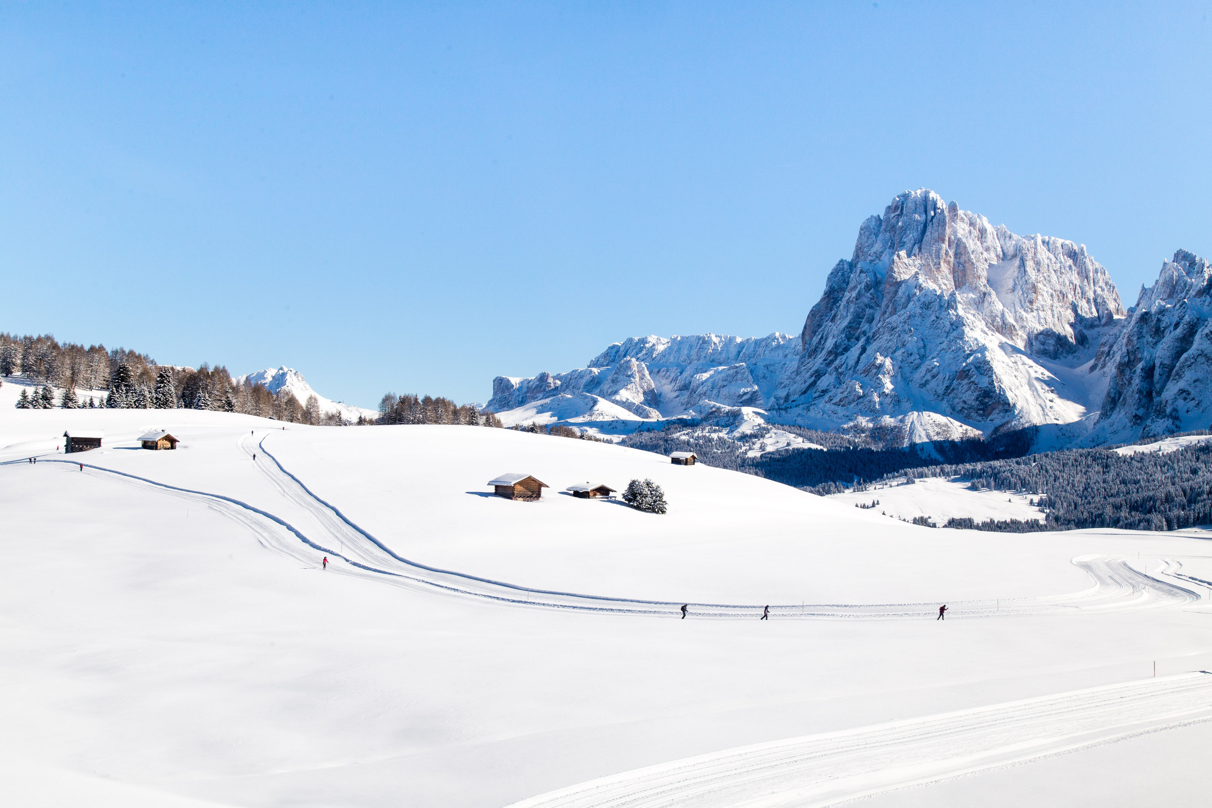 Cross-country skiers on a snow-covered mountain pasture with alpine huts and panoramic mountain views
