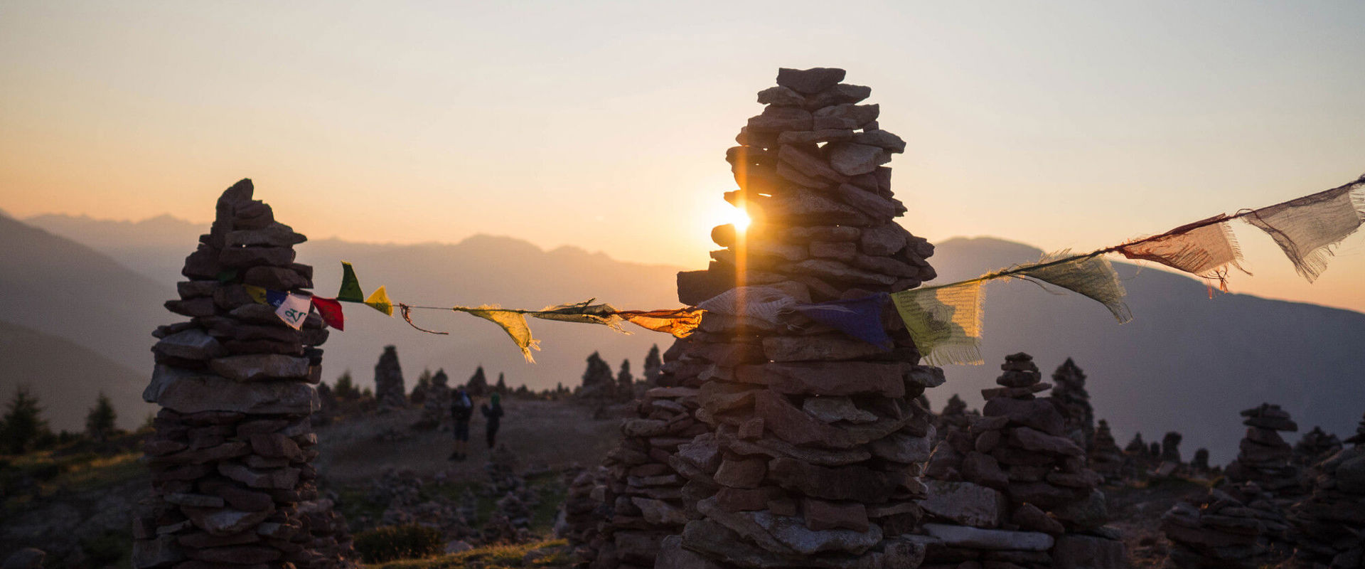 Stone figures Stoanerne Mandln and prayer flag on the mountain top at sunrise or sunset.