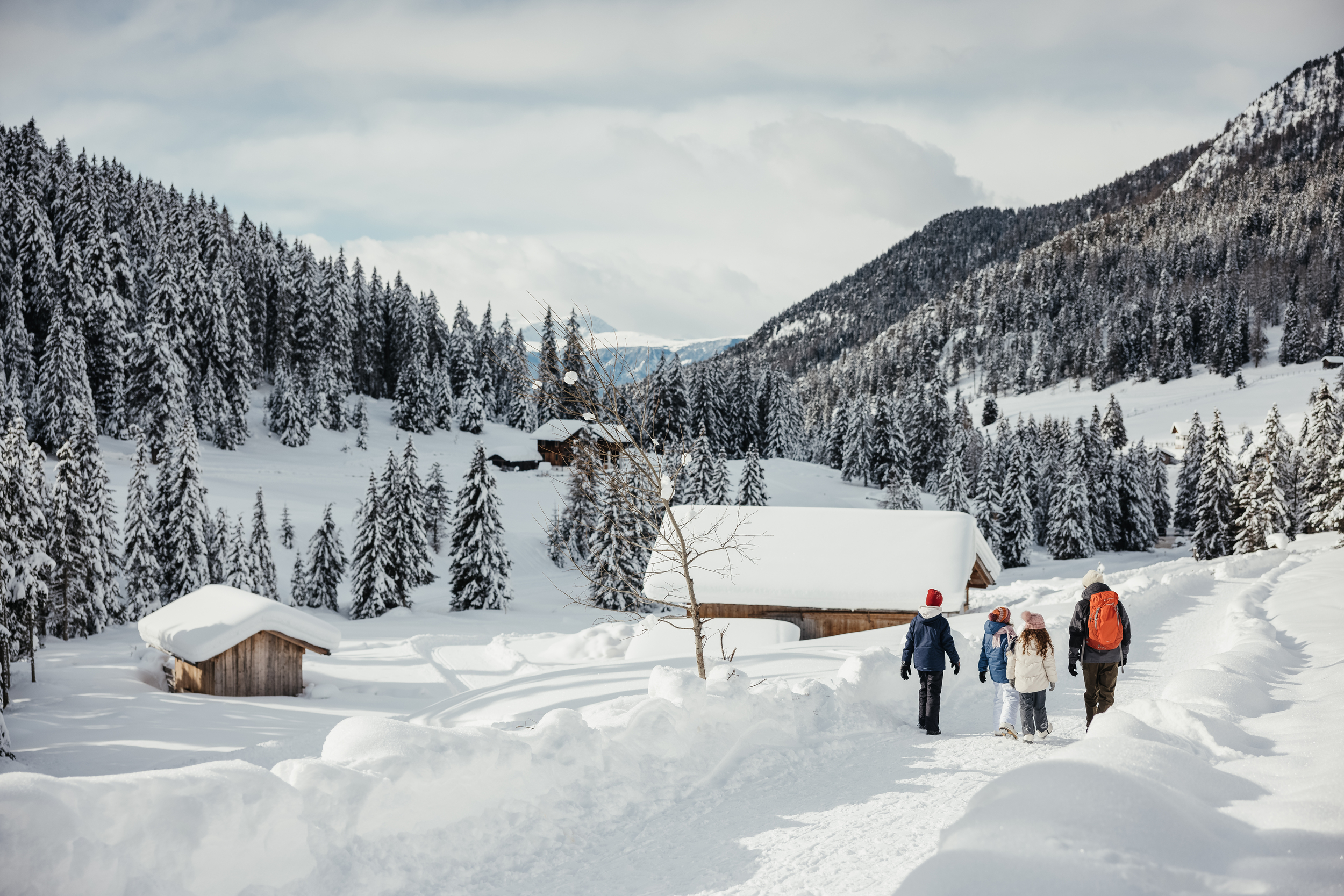Family hiking on a winter hiking trail through a snowy landscape with mountain huts.